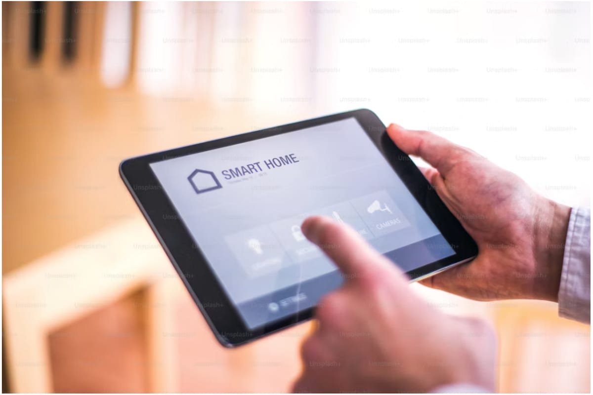 A hand using a smart home app on a tablet to control lighting, security and cameras